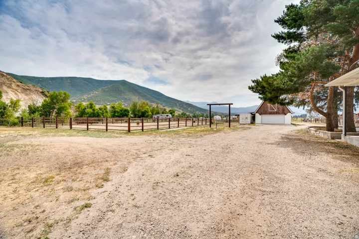 Expansive gravel drive encompassing a fenced-in riding arena and a rustic barn with a white garage door
