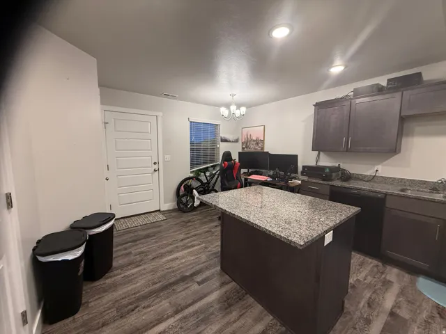 Kitchen featuring an island with a speckled countertop, dark wood-finish cabinetry, wood-finish flooring, and recessed lighting