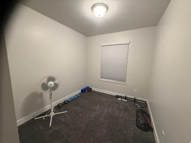Interior room featuring neutral wall finishes, dark textured carpeting, and a single window with horizontal blinds