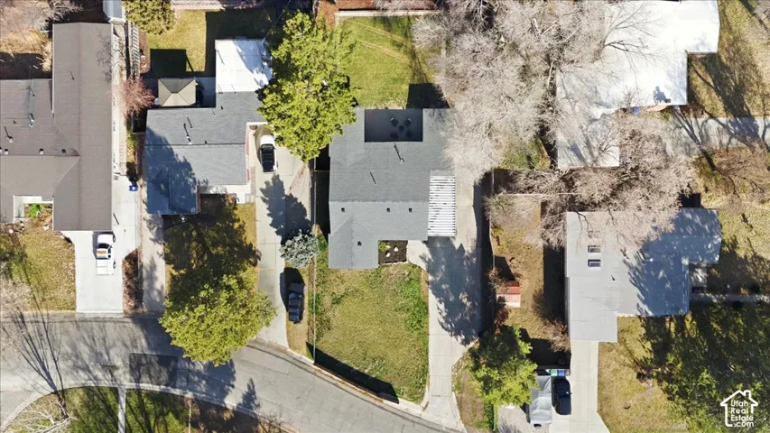 Property featuring a dark-toned roof, an expansive grassy front yard, mature perimeter trees, and a concrete driveway