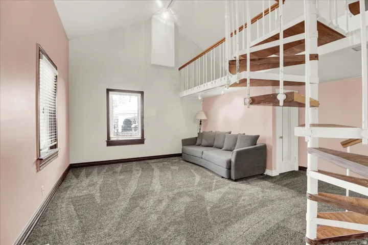 Spiral staircase with wood-finish treads and white risers, complementing the vaulted ceiling and gray carpeting