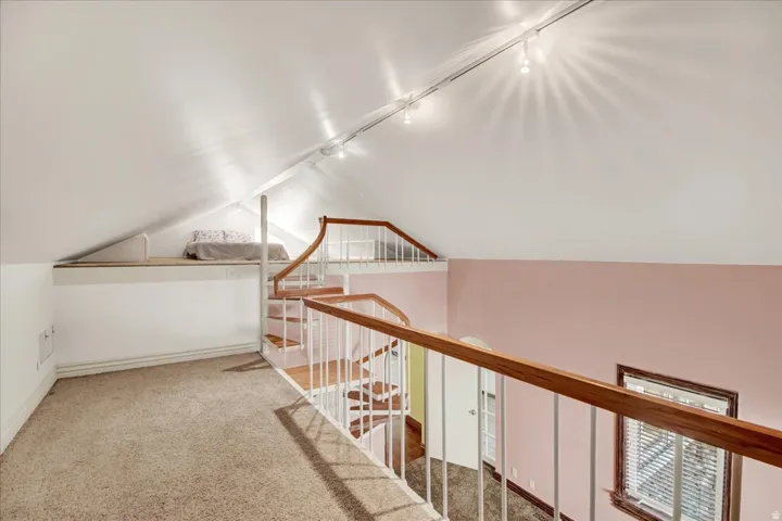 Upper level loft space with track lighting, sloped ceilings, and wood-finish handrails