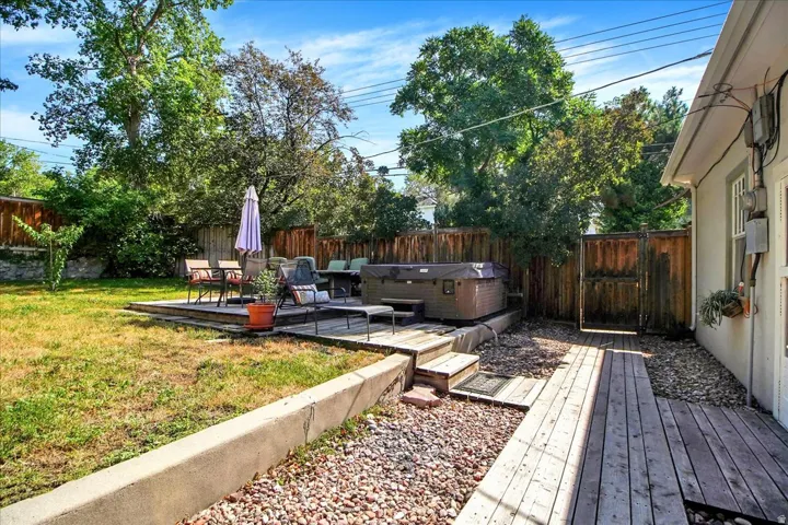 Spacious backyard featuring a wooden deck with a built-in hot tub, a privacy fence, mature trees, and a wooden walkway