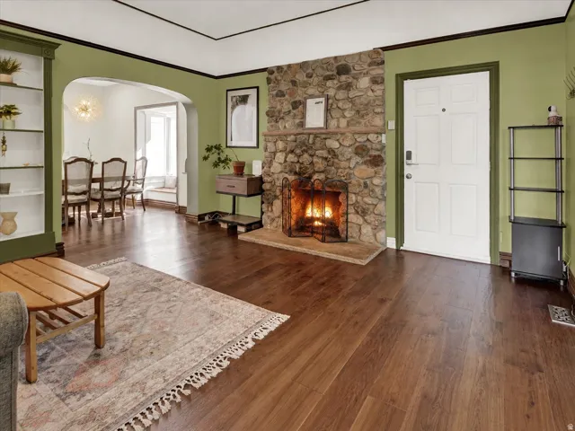 Living area featuring a stone fireplace with a wood mantel, wood-finish flooring, and an arched entry to an additional room