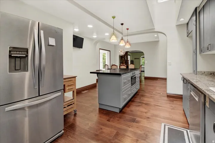 Kitchen featuring a stainless steel refrigerator, wood-finish flooring, a central island with integrated oven, pendant lighting, and arched doorways