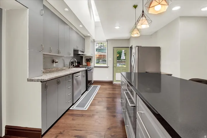 Kitchen featuring a large island with a dark countertop, grey cabinetry, stainless steel appliances, wood-finish flooring, and recessed lighting