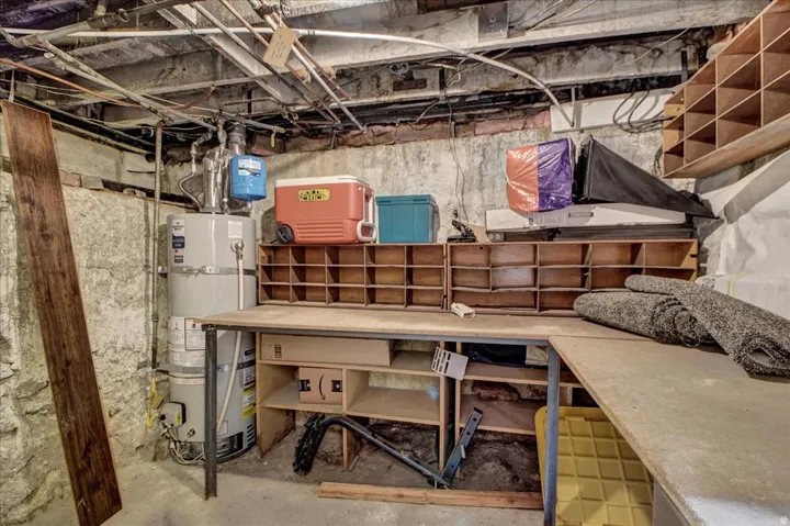 Utility area featuring a water heater, exposed piping, and a workbench with integrated shelving