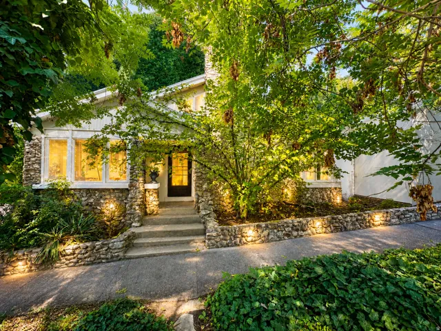 Stone façade exterior with a dark-paneled entry door, multiple large windows, and a concrete walkway.  Virtually enhanced.