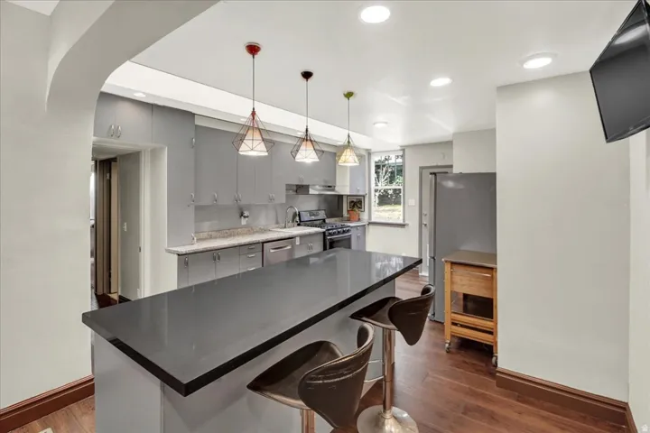 Kitchen featuring a dark countertop island, modern pendant lighting, recessed ceiling lights, gray cabinetry, and wood-finish flooring