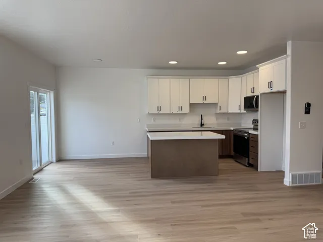 Kitchen featuring a central island with a solid surface countertop, white shaker-style cabinetry, stainless steel appliances, and wood-finish flooring
