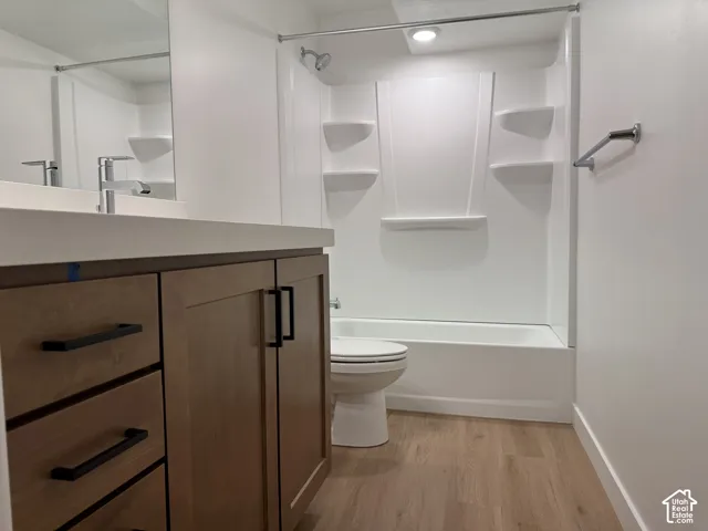 Bathroom featuring a wood-finish vanity with matte black hardware, solid surface countertop, wood-finish flooring, and a white tub-shower combination with built-in shelving
