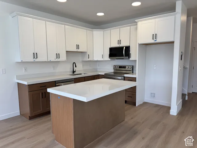 Kitchen featuring two-tone cabinetry, central island with quartz countertop, recessed lighting, stainless steel appliances, and wood-finish flooring