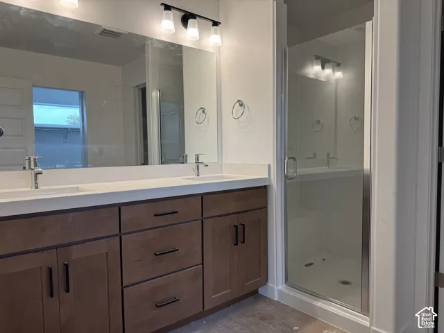 Dual vanity with white countertops and undermount sinks, brown wood-finish cabinetry, and a walk-in shower with a clear glass enclosure