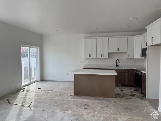 Kitchen featuring white upper cabinetry, lower wood-finish cabinetry, and a central island with a solid surface countertop