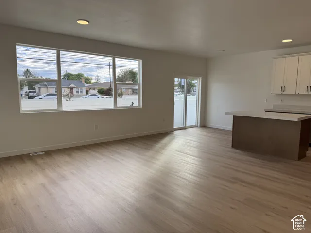 Open-concept interior featuring wood-finish flooring, recessed lighting, expansive picture window, sliding glass door, and kitchen peninsula with light-toned countertop and white upper cabinetry
