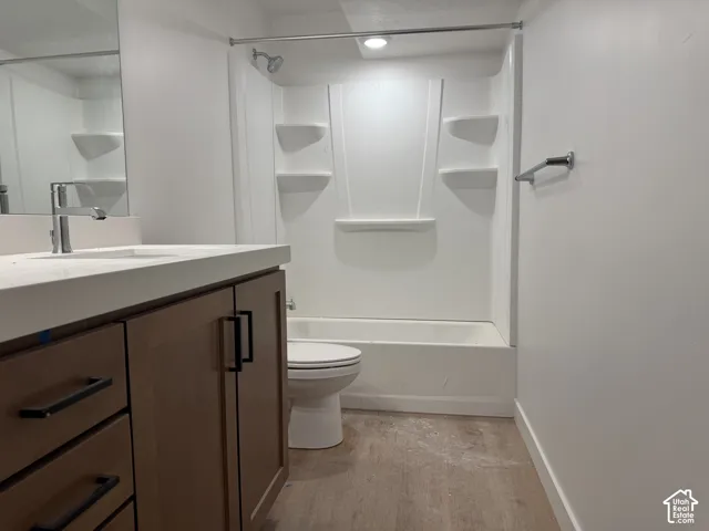 Integrated shower and bathtub unit, light wood-finish flooring, vanity with light countertop, chrome faucet, and brown cabinetry with dark hardware