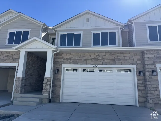 Stone veneer facade with light gray siding, white garage door with window inserts, and a covered entryway