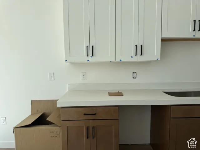 White upper cabinetry with black hardware, light-toned countertop, and wood-finish lower cabinetry with black hardware