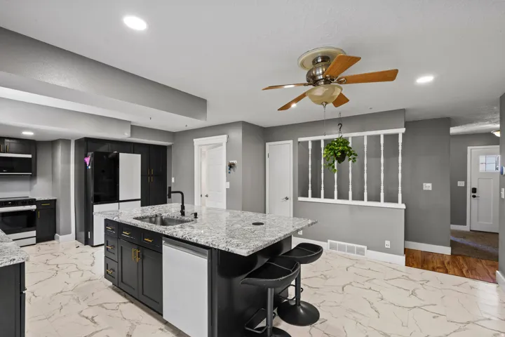 Kitchen featuring an island with a sink, granite countertops, dark cabinetry, and white tile flooring