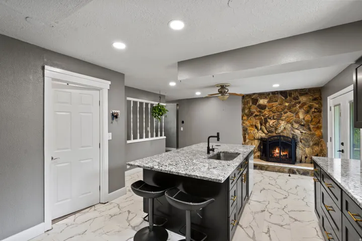 Kitchen island with a built-in sink and seating, stone accent wall, fireplace, recessed lighting, and wood-finish flooring