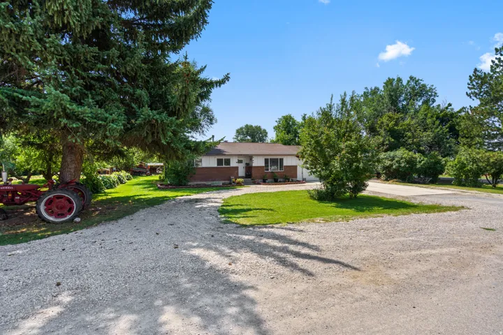 Ranch-style exterior with brick and siding facade, gravel driveway, mature trees, and manicured landscaping