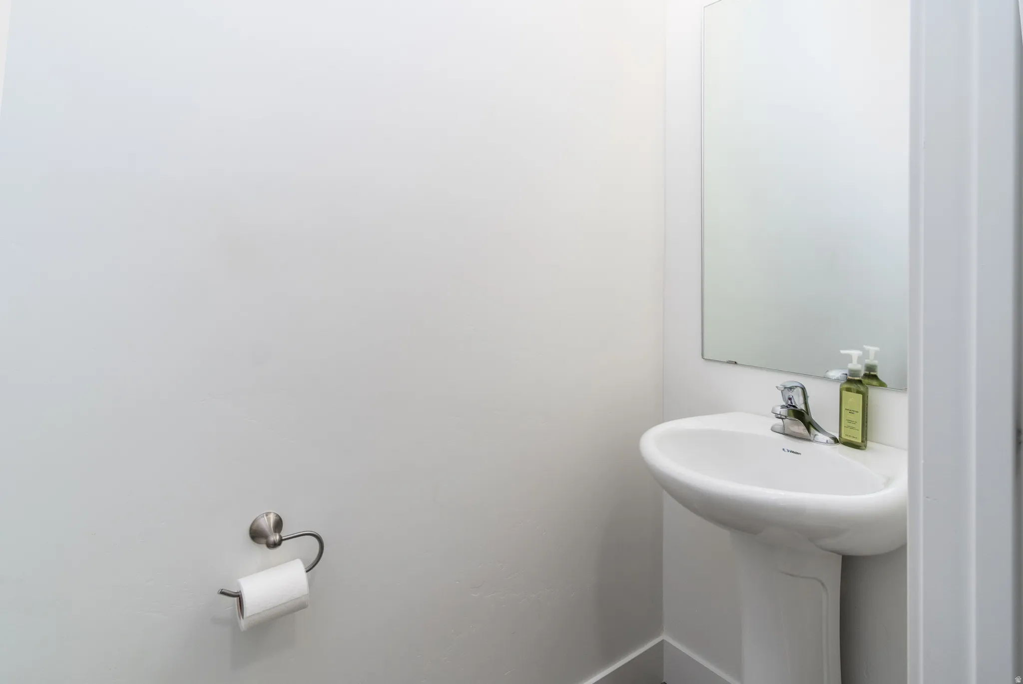 Pedestal sink with chrome faucet, wall-mounted mirror, and neutral wall tones