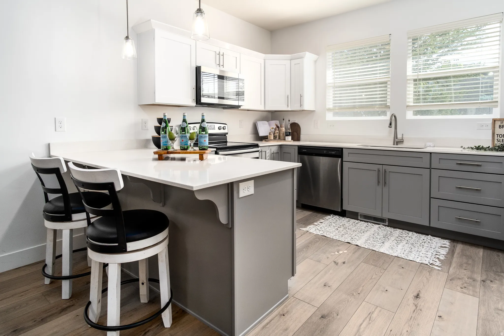 Contemporary kitchen featuring wood-finish flooring, two-tone cabinetry with white upper and gray lower cabinets, quartz countertops, and stainless steel appliances