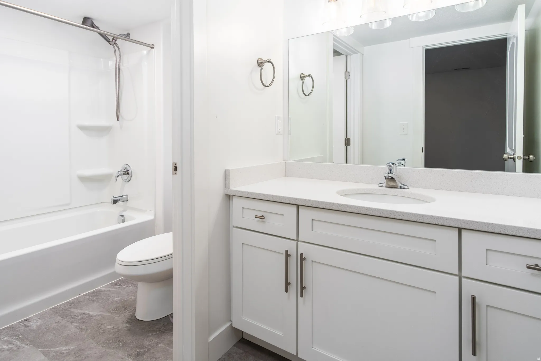 Bathroom featuring a white vanity with an integrated sink, polished chrome faucet, and a large mirror with overhead lighting