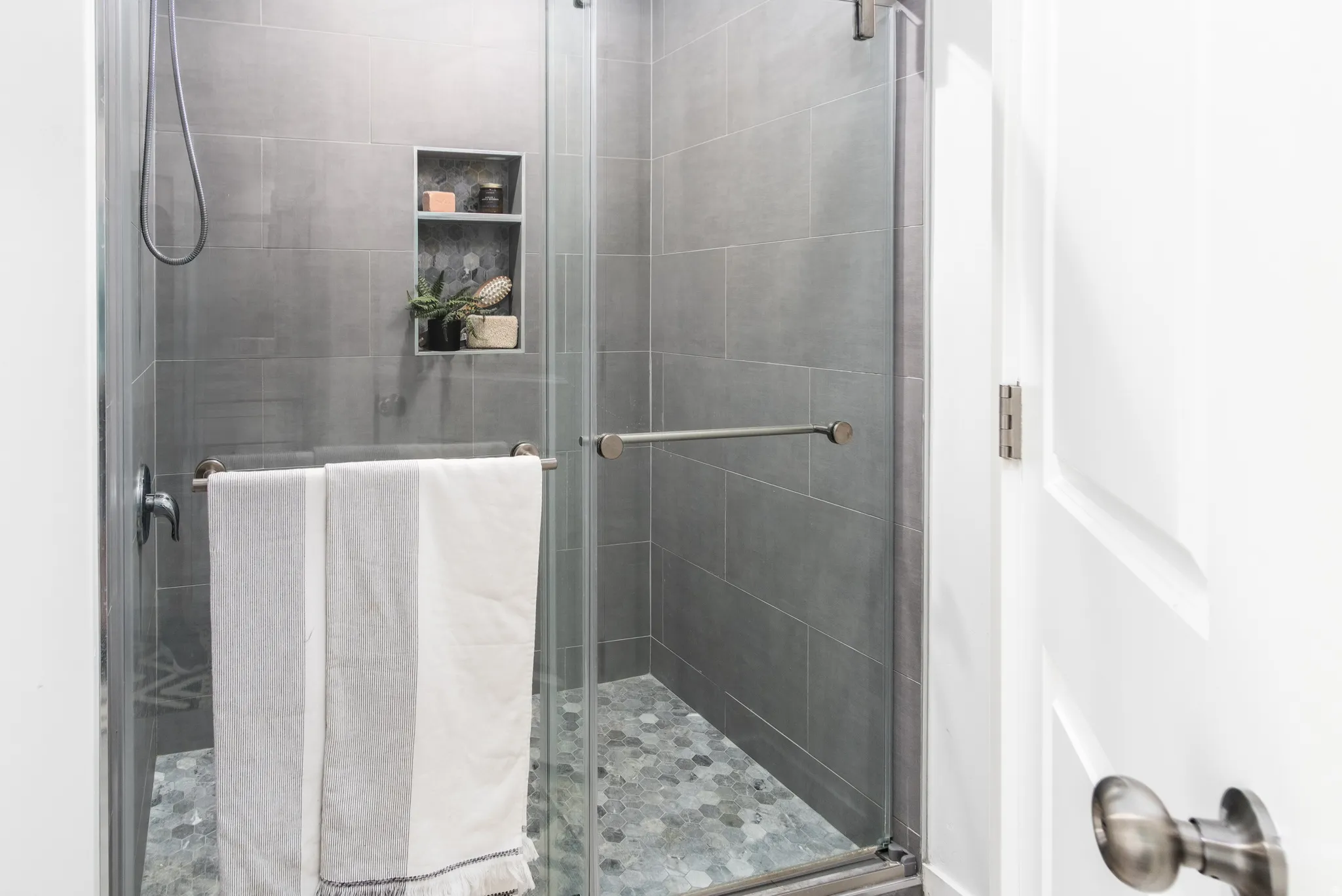Glass-enclosed shower featuring large format gray wall tile and a hexagonal pebble tile floor