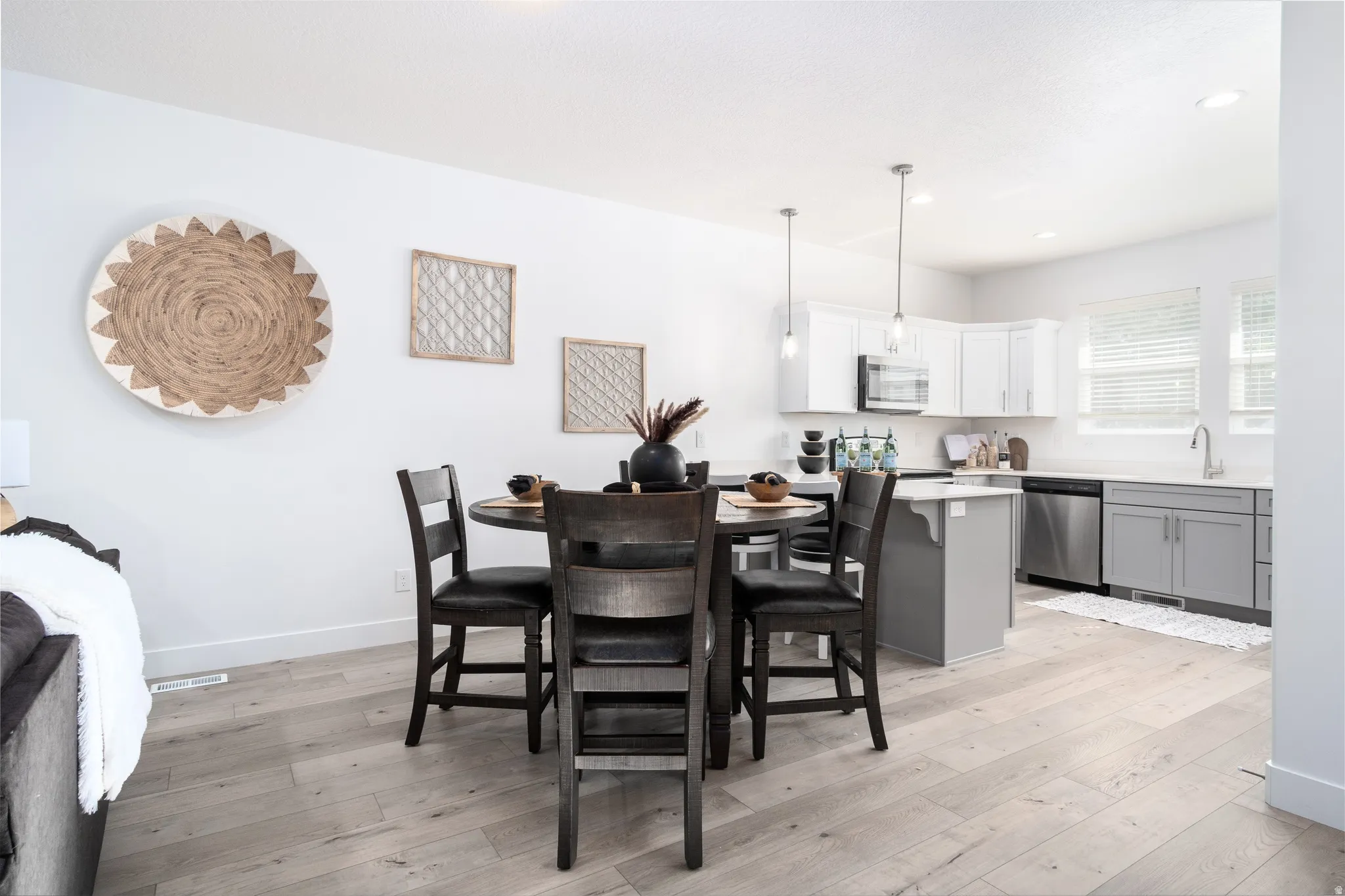 Open-concept kitchen featuring white upper cabinetry, gray lower cabinetry, stainless steel appliances, and light wood-finish flooring