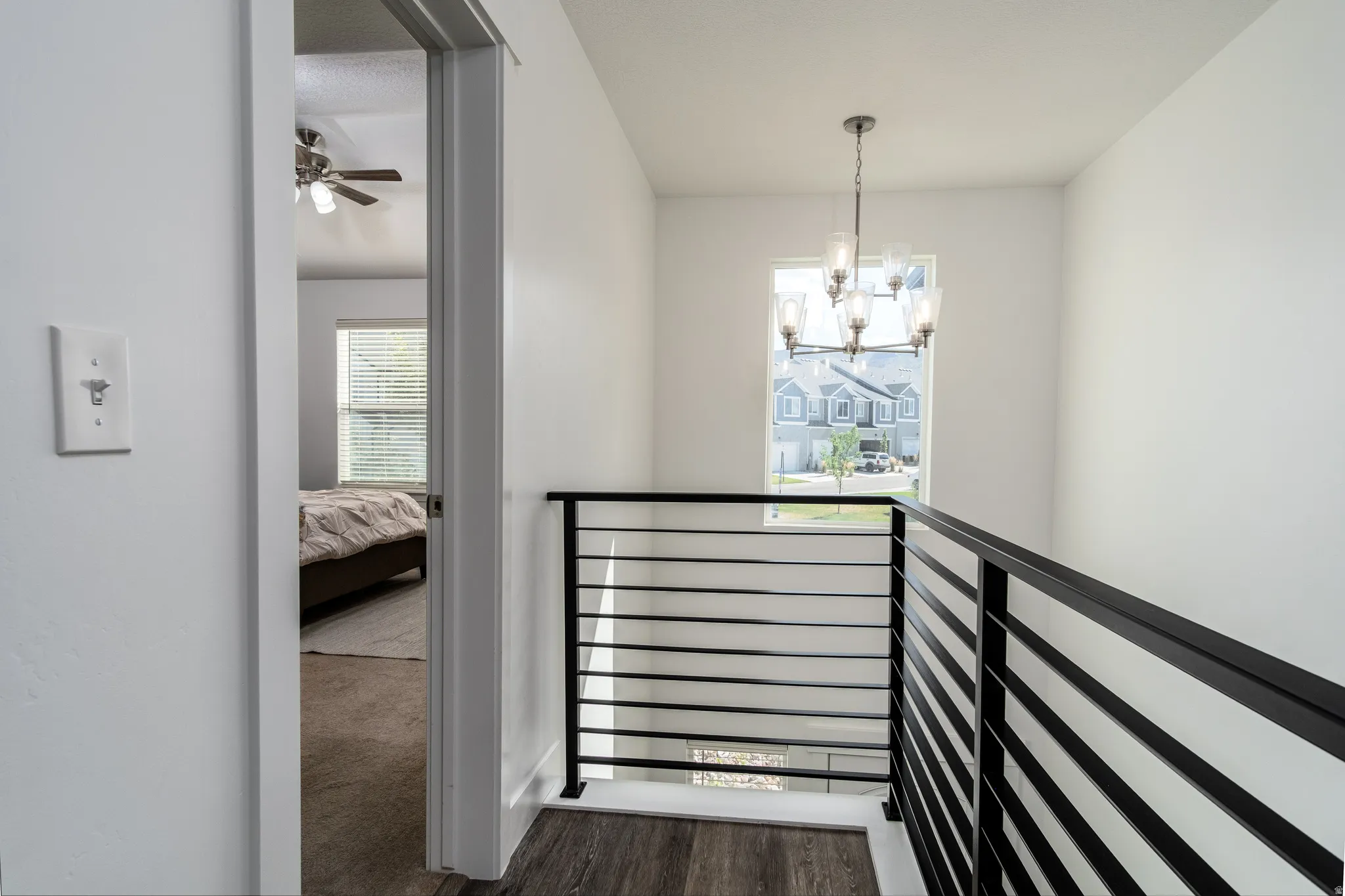 Upper landing featuring a contemporary chandelier, horizontal metal stair railing, and wood-finish flooring