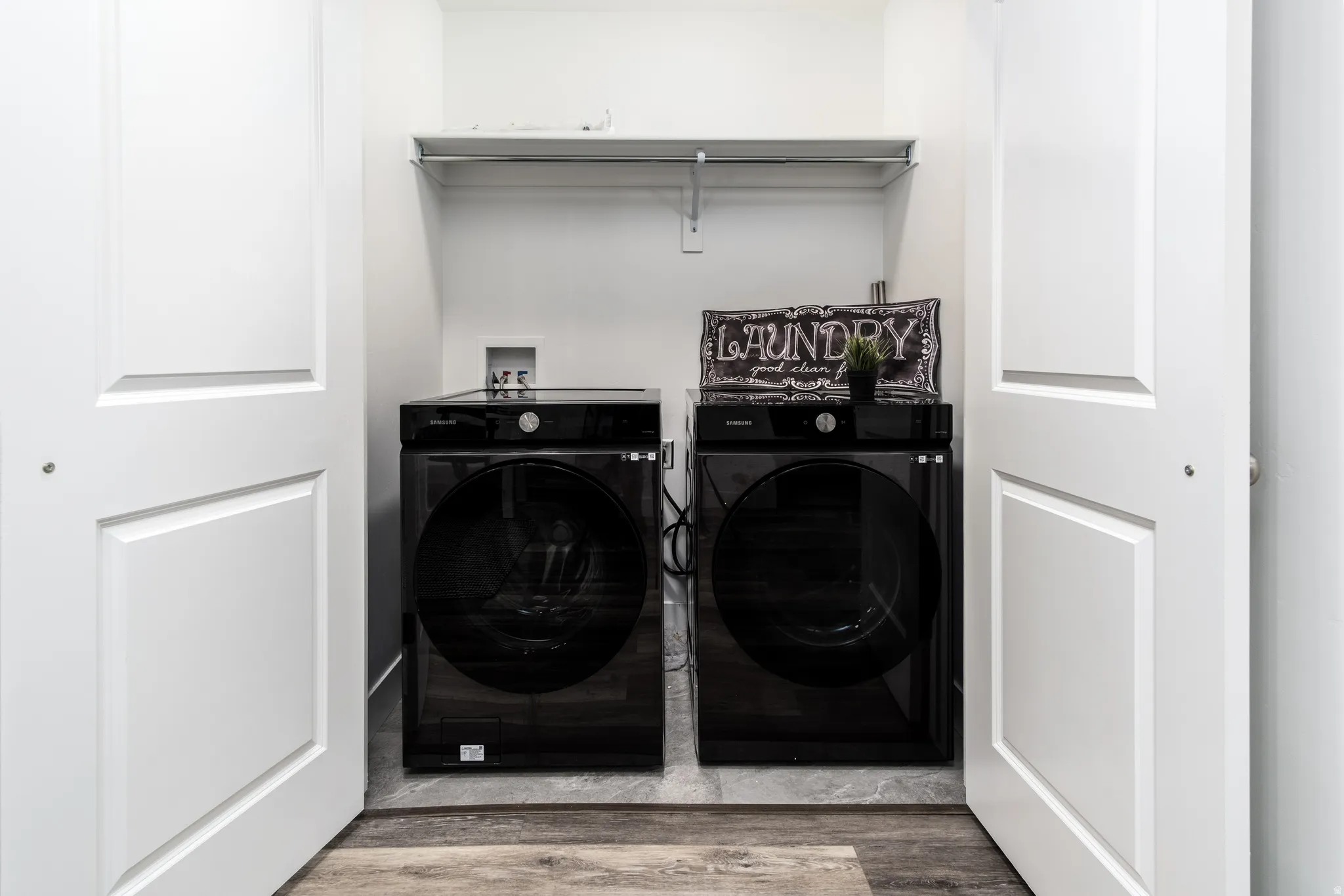 Dedicated laundry closet featuring a built-in shelf, white paneled bifold doors, and wood-finish flooring