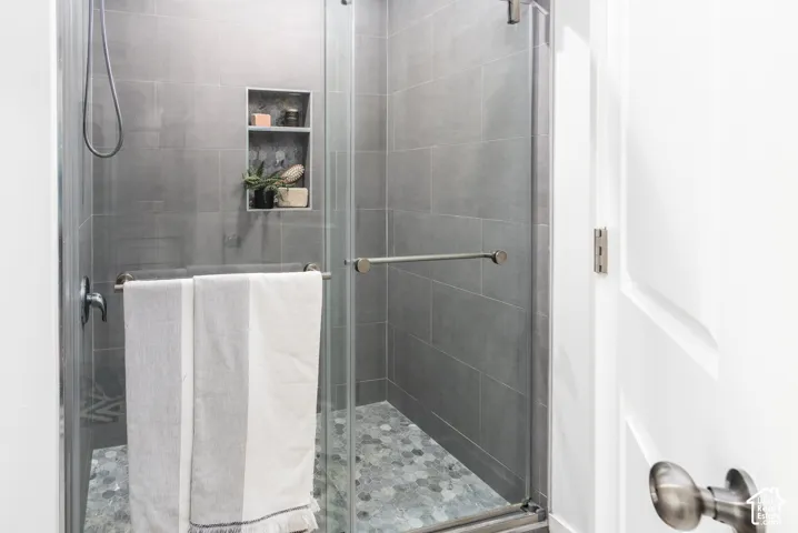Glass-enclosed shower featuring large format gray wall tile and a hexagonal pebble tile floor