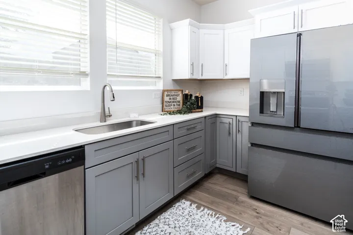 Contemporary kitchen featuring light gray base cabinetry, white upper cabinetry, light-toned countertops, a stainless steel sink with a gooseneck faucet, and integrated stainless steel appliances