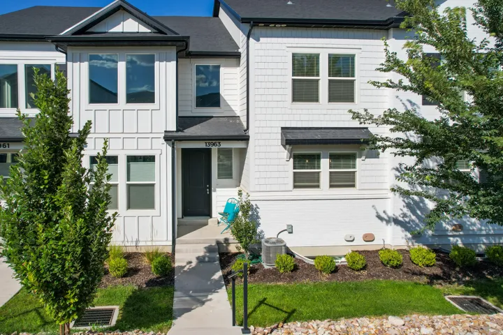 Modern townhome exterior featuring white vertical siding, dark roof, and mature landscaping