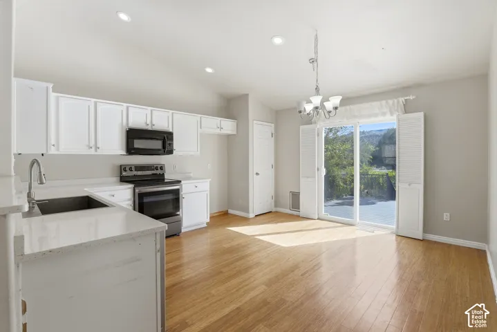 Vaulted ceilings, wood-finish flooring, white cabinetry, stainless steel appliances, and a sliding glass door