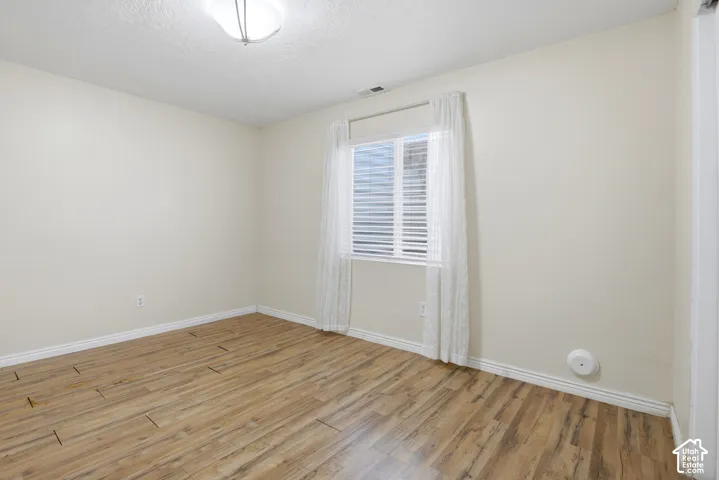 Recessed window with horizontal blinds, wood-finish flooring, ceiling-mounted light fixture, and neutral wall paint