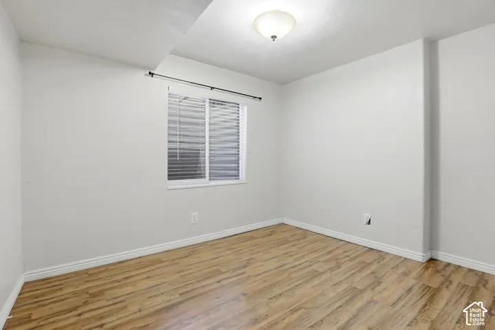 Wood-finish flooring, white walls, single window with blinds, and a flush mount ceiling light fixture