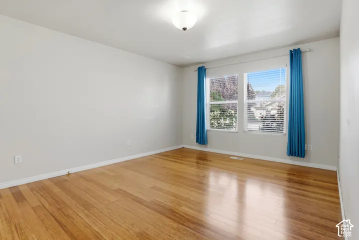 Hardwood flooring with a smooth finish, two windows featuring blinds, and a flush mount ceiling light fixture