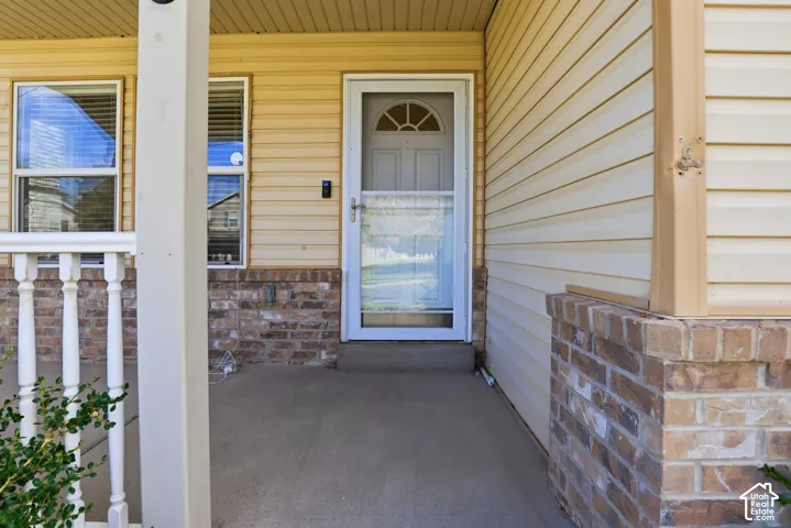 Front porch with concrete flooring, white balusters, brick accent wall, and beige siding