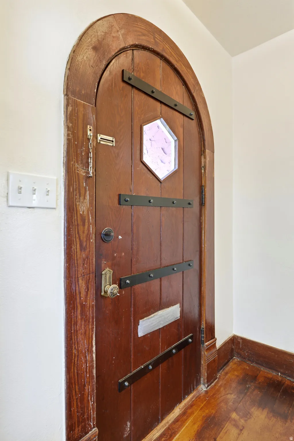 Arched wooden door with decorative metal strapping and an octagonal stained glass inset