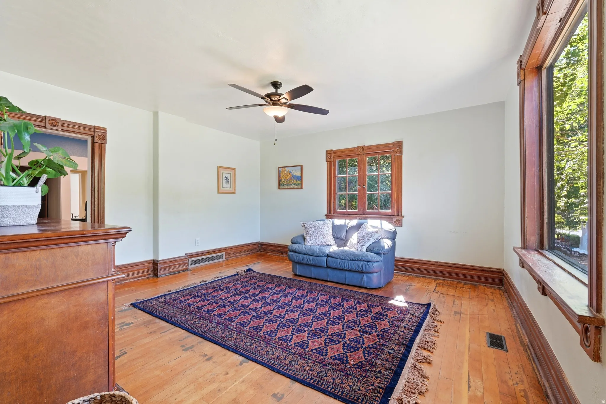 Light-filled room featuring wood-finish flooring, white walls, and a ceiling fan