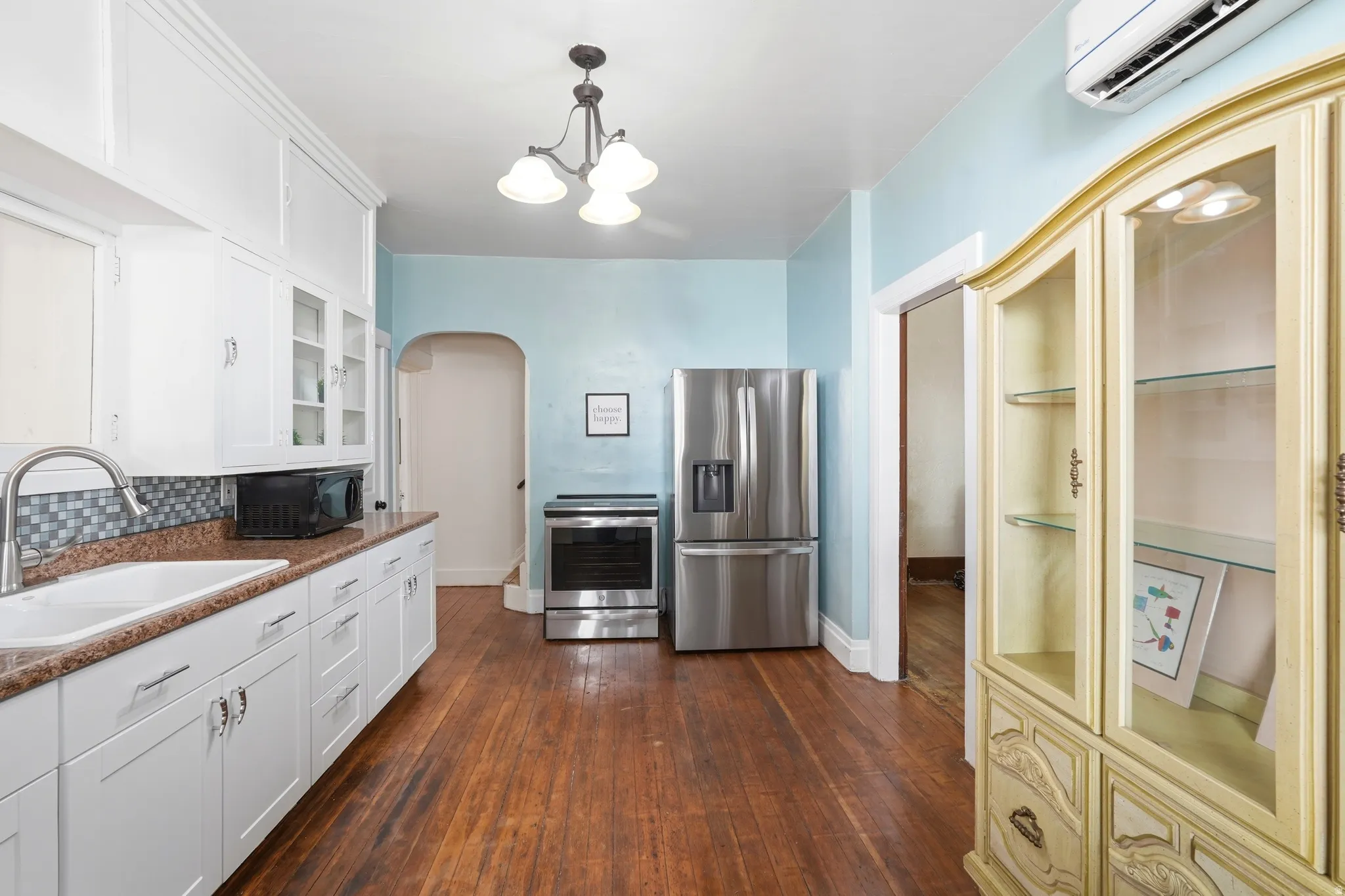 Kitchen featuring wood-finish flooring, white cabinetry with display uppers, a stainless steel refrigerator, and a mosaic tile backsplash