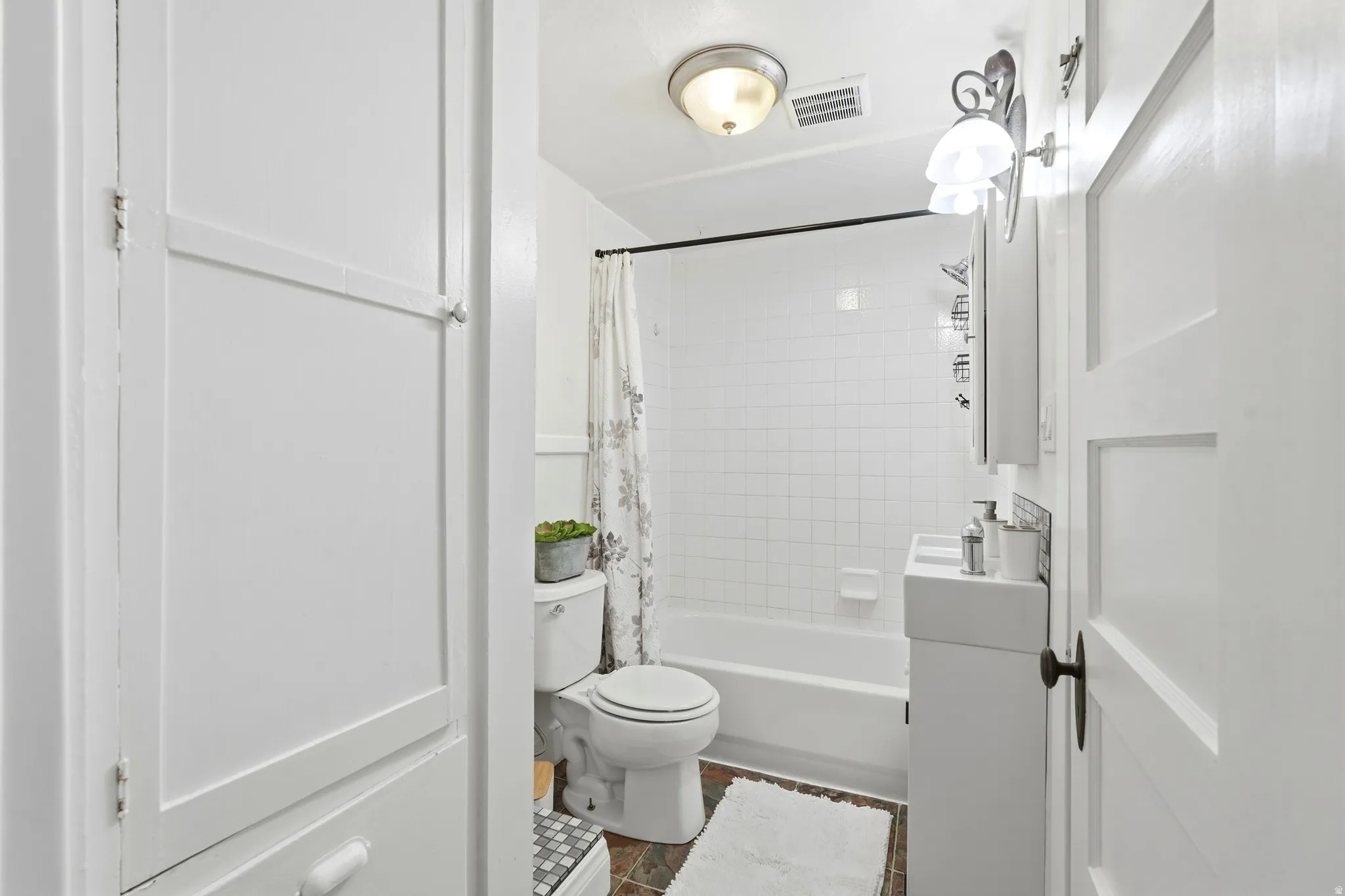 White-tiled bath and shower combination with dark-toned flooring