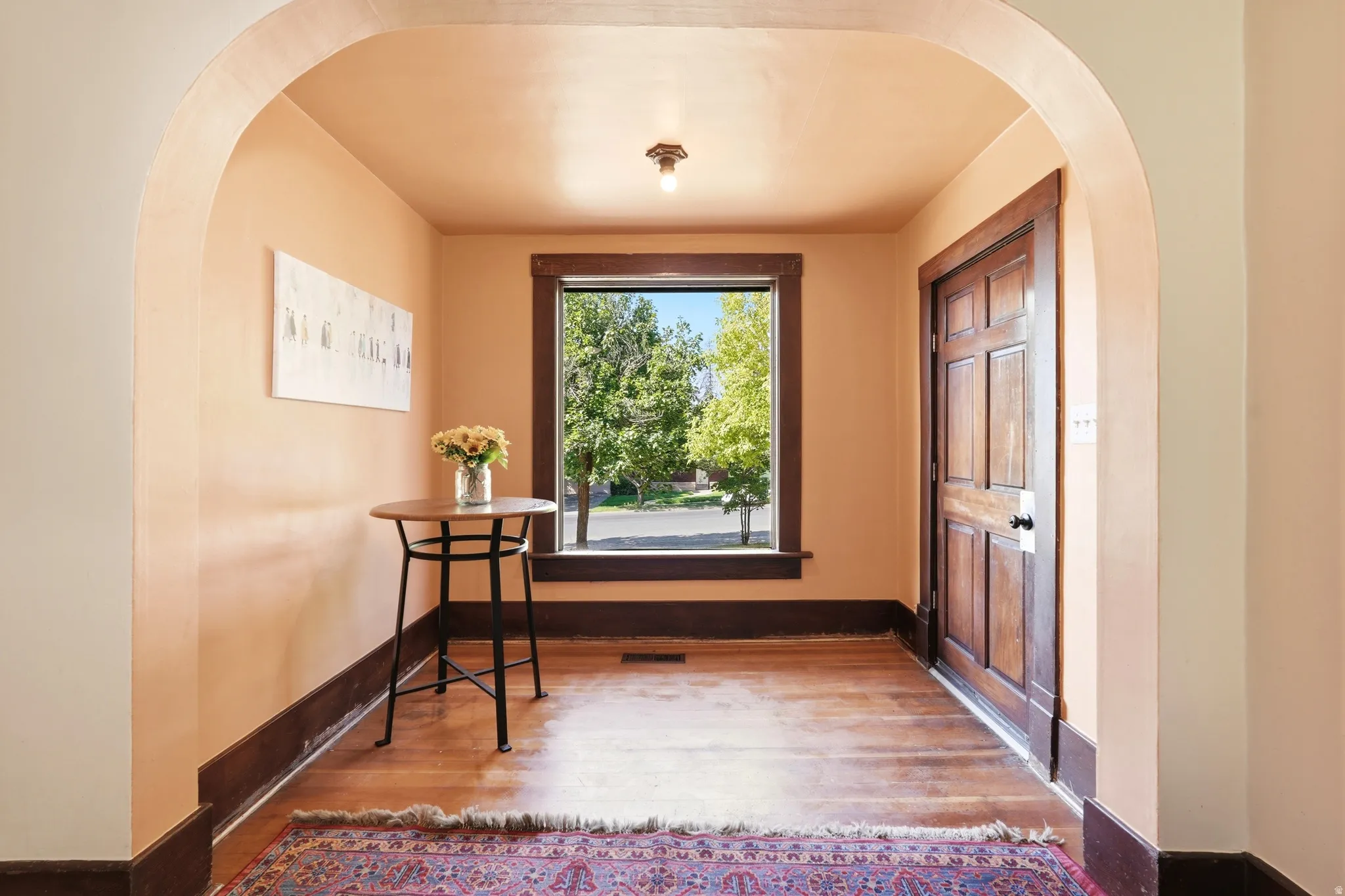 Archway entry featuring hardwood flooring, a multi-paneled wood door, dark wood trim, and a window with exterior views