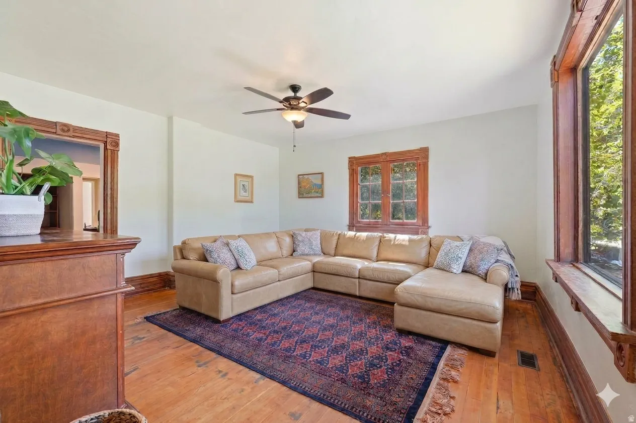 Living area featuring wood-finish flooring, white walls, and a ceiling fan
