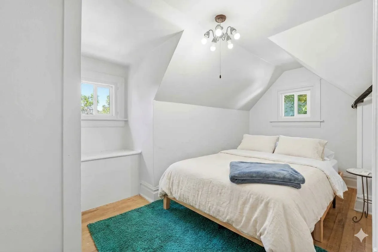 Attic room featuring sloped ceilings, two windows with white trim, and light wood-finish flooring
