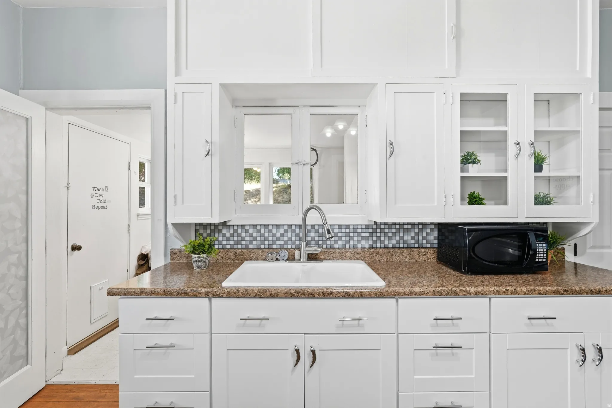 White cabinetry with glass-front display cabinets, mosaic tile backsplash, and a double-basin sink with a gooseneck faucet