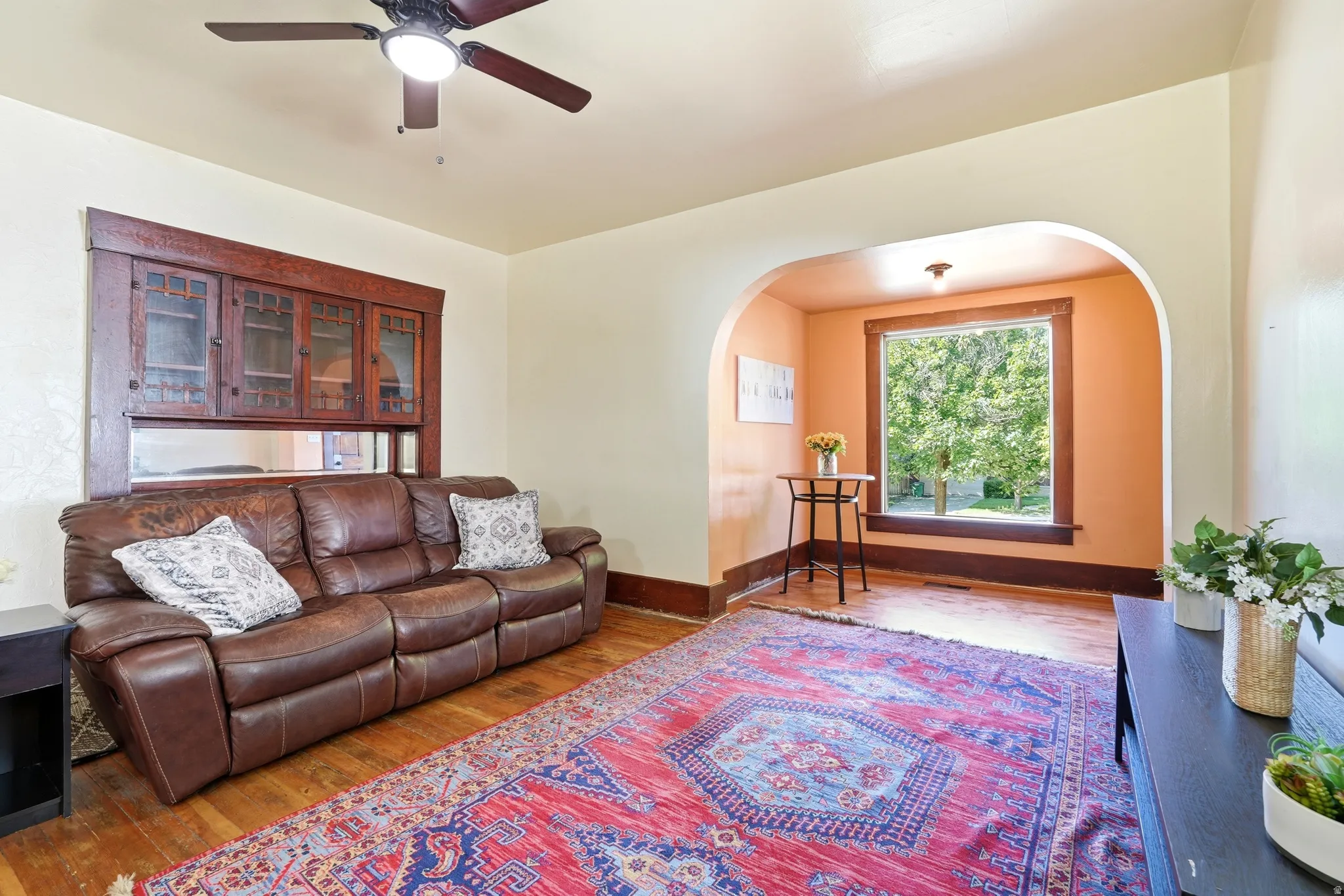 Living area featuring wood-finish flooring, a ceiling fan with integrated lighting, and an arched doorway