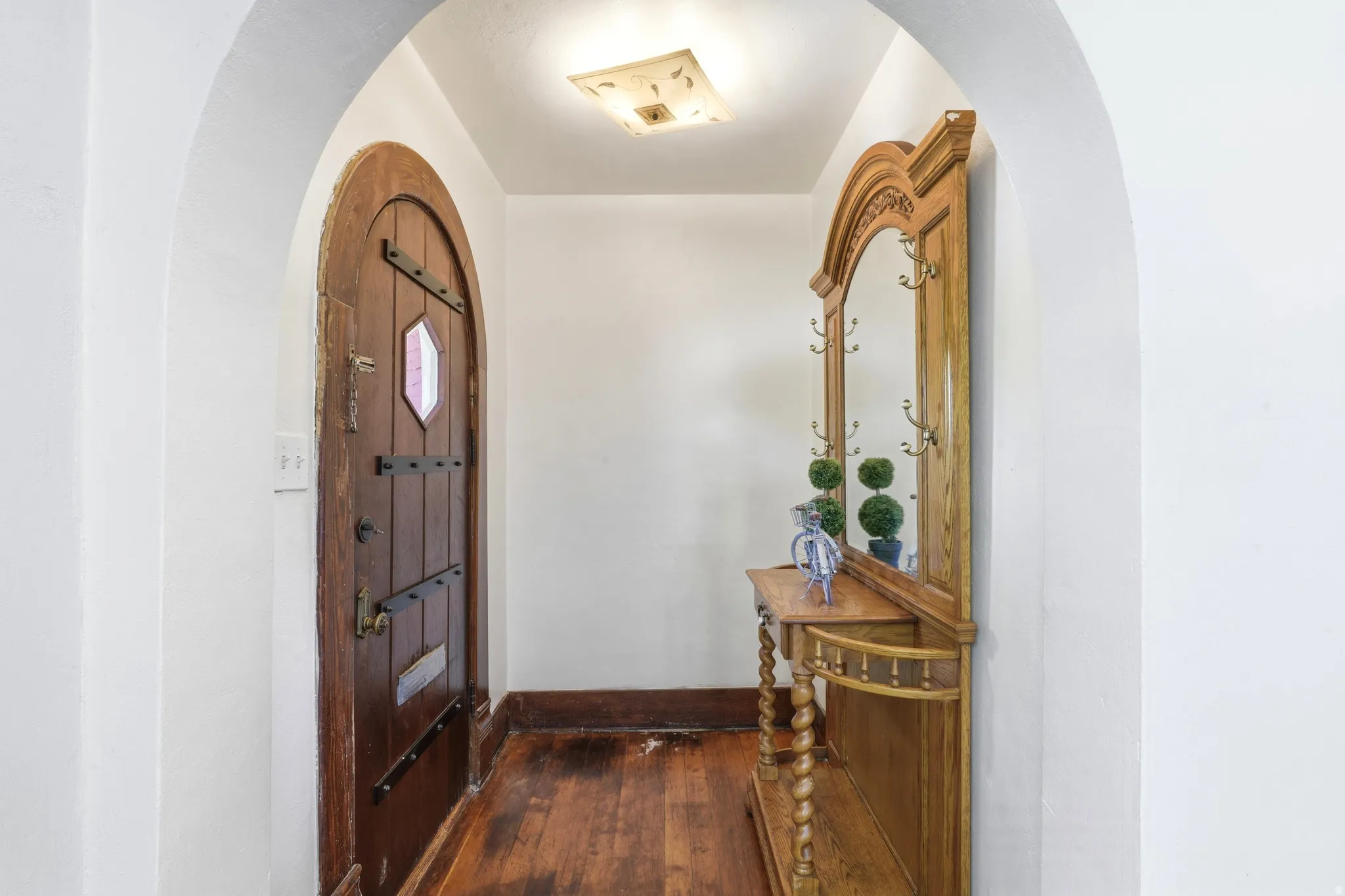 Arched doorway entry featuring wood-finish flooring, a decorative ceiling light fixture, and a solid wood entry door with an arched top and hexagonal window
